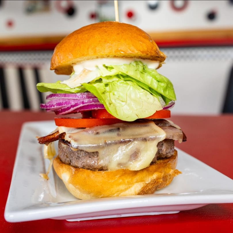 A tall Bergstrom's Burger with bacon, melted cheese, tomato, red onion, lettuce, and mayonnaise.