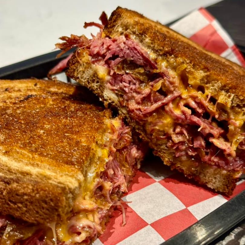 A grilled sandwich, cut in half, revealing melted cheese and shredded meat on checkered paper.